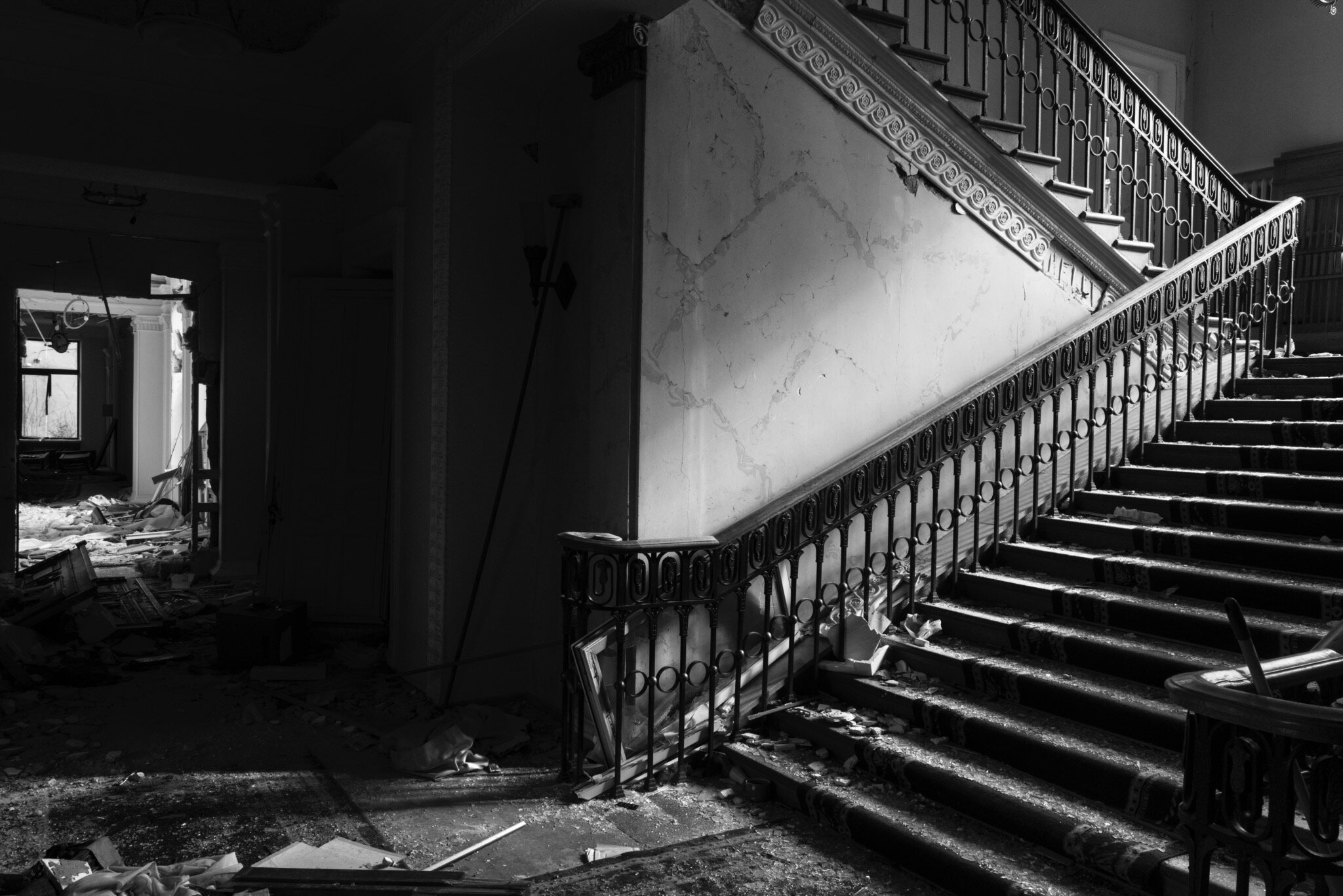 A dark black and white shot of a dilapidated staircase that is covered in debris. 